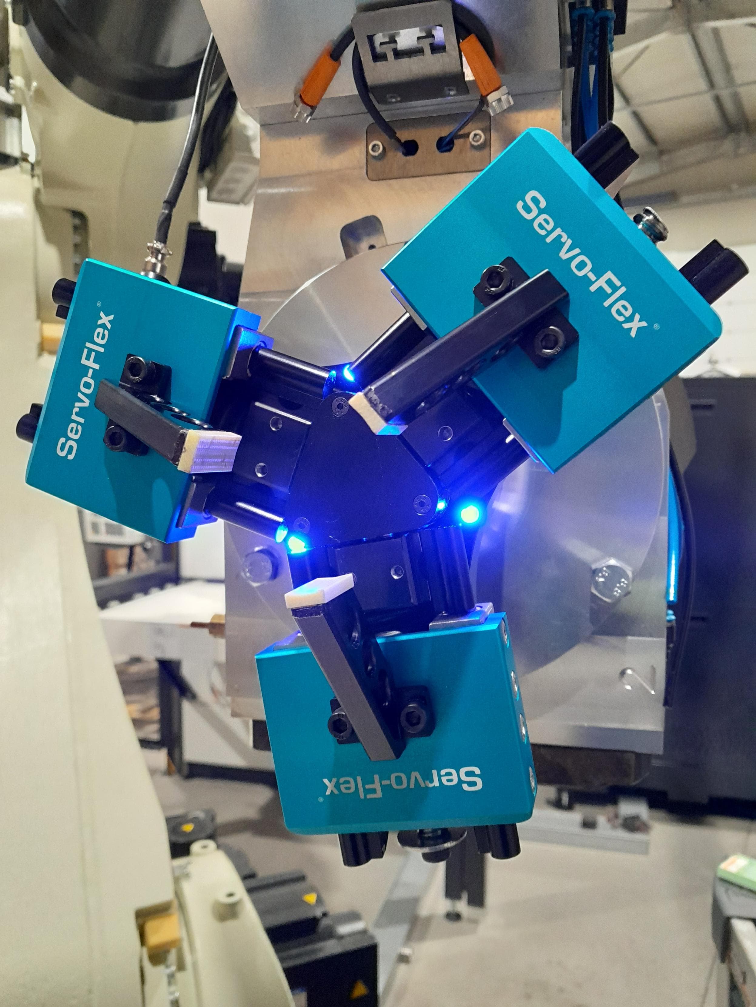 A Servo-Flex gripper mounted on a robot, holding a machined part