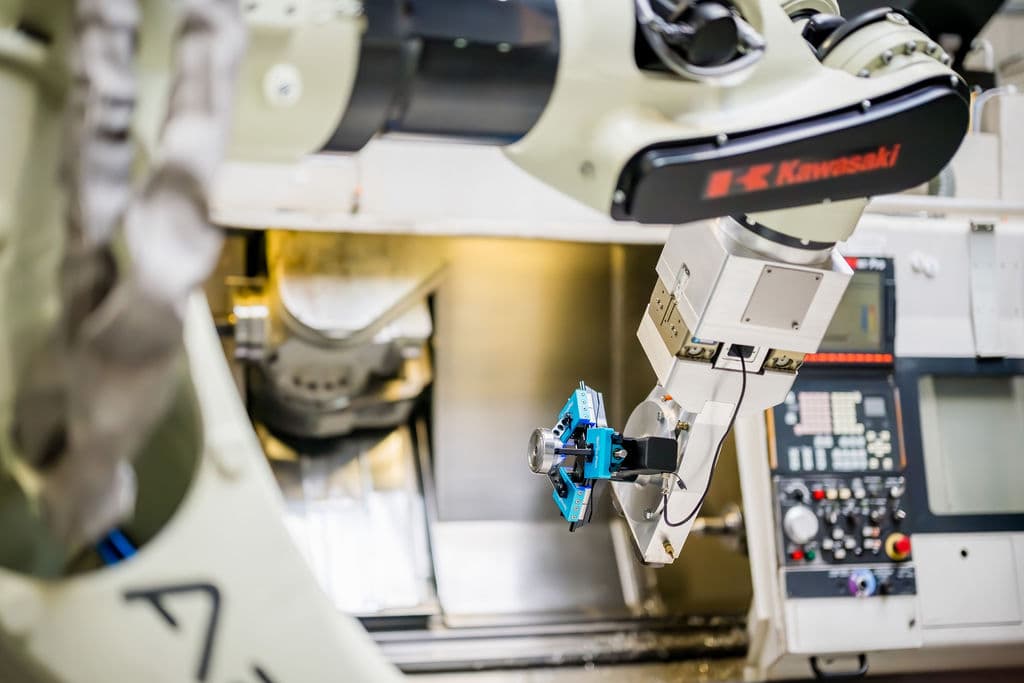 Un robot Kawasaki portant une pièce usinée — la charge utile au service de la pièce, pas du préhenseur